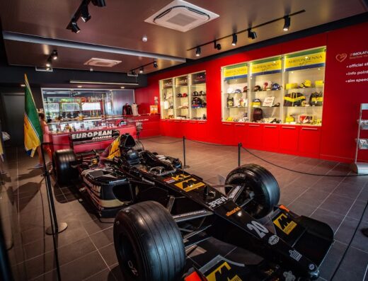 Interno del negozio IF Imola Faenza Tourism Company con esposizione di una monoposto di Formula 1 nera e oro, caschi di Ayrton Senna e accessori racing.