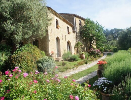 Il Cantico Della Natura Eco Resort: Stone building with arched doorways surrounded by lush gardens with roses and a stone pathway.