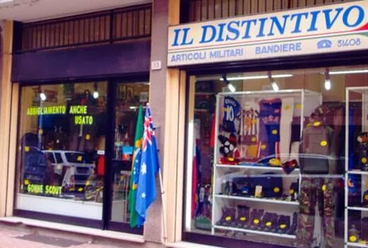 Foto del negozio "Il Distintivo" con articoli militari, bandiere e abbigliamento anche usato. Vetrina con esposizione di accessori e divise.