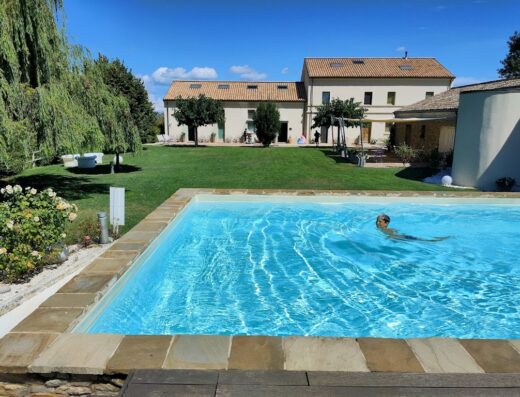 Il Gallo Senone Resort di campagna: Piscina con un bambino che nuota, prato verde curato e casale ristrutturato sullo sfondo, ideale per vacanze rilassanti.