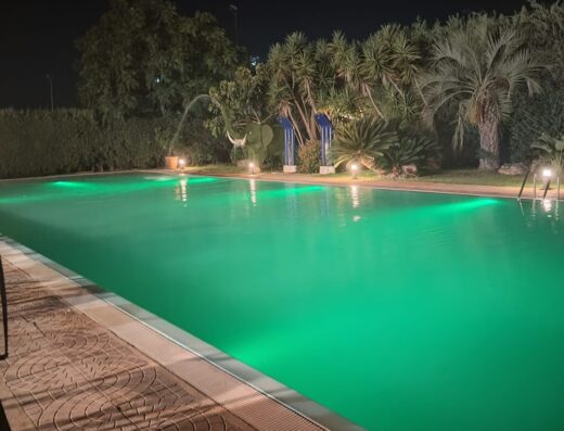 Vista notturna della piscina illuminata presso Il Giardino dei Pavoni, con vegetazione lussureggiante e decorazioni eleganti.