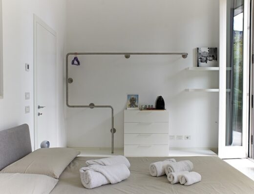 Camera luminosa de Il Giardino Segreto con letto, comodino bianco, appendiabiti in metallo, e porta finestra aperta.