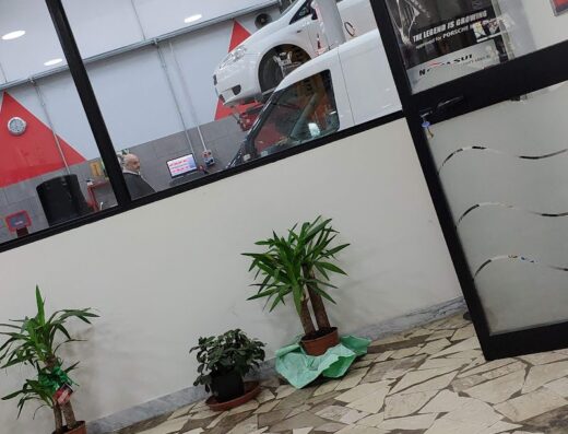 Interno di "Il Gommista", con auto su ponte sollevatore, scaffali di pneumatici Nexen e pavimentazione in pietra. Servizi di riparazione e sostituzione pneumatici per auto e moto.