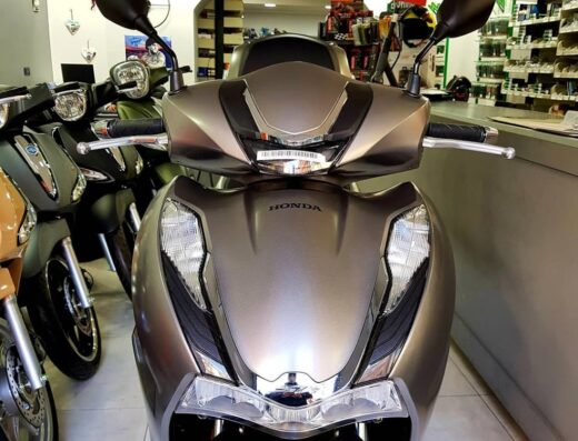 Primo piano di uno scooter Honda grigio in un negozio di ricambi e accessori moto. Vetrina di accessori per motocicli sullo sfondo.