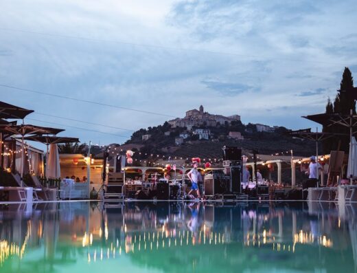Il Sapore della Luna: Vista di una piscina illuminata con un palco per musica dal vivo sullo sfondo di un borgo collinare in Italia.