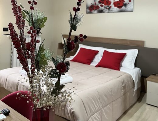 Accogliente camera da letto matrimoniale in un B&B ILBE, con arredi curati, cuscini rossi e decorazioni floreali, ideale per un soggiorno rilassante e confortevole.