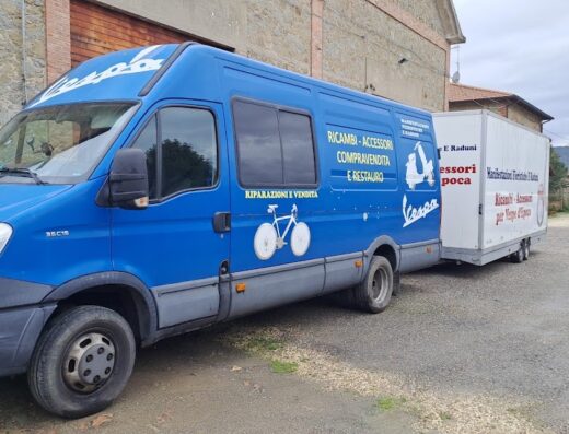 Furgone blu per trasporto moto d'epoca e accessori Vespa, con rimorchio pubblicitario, parcheggiato in strada. Servizi di riparazione, vendita e restauro.