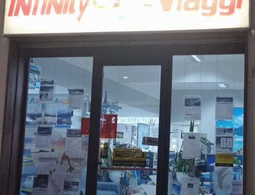 Vetrine dell'agenzia viaggi Infinity Viaggi con manifesti di destinazioni turistiche e promozioni di servizi di viaggio