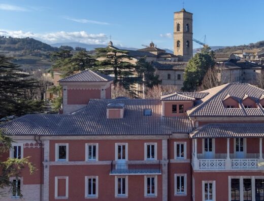 Veduta panoramica di un edificio storico con tetto in tegole a Urbino, Marche, Italia, con torre campanaria sullo sfondo e colline circostanti.