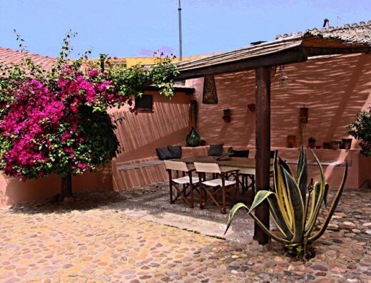 Un cortile accogliente a Is scabas Guestrooms, con tavolo, sedie e bougainvillea fiorita. Ideale per un soggiorno rilassante.