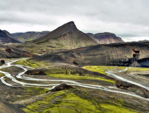 Paesaggio islandese con fiume serpeggiante tra montagne e vegetazione verde, ideale per viaggi in moto e avventure su due ruote