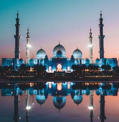 La Moschea Sheikh Zayed di Abu Dhabi illuminata al crepuscolo, riflessa nell'acqua, un'icona di architettura islamica per viaggi e turismo.