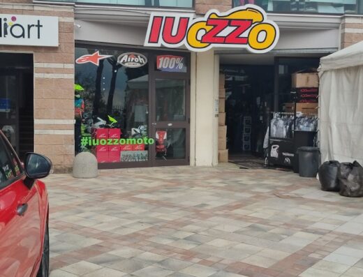 Foto del negozio Iuozzo, rivenditore di abbigliamento, calzature, accessori e DPI per la sicurezza motociclistica. Insegna luminosa e vetrine con caschi Airoh e abbigliamento tecnico moto.