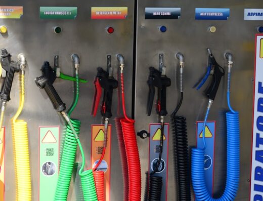 Dettaglio di una stazione di autolavaggio iWASH per moto, con pistole a spruzzo per pulizia antibatterica, lucidatura cruscotti, detergente vetri, nero gomme, aria compressa e aspirazione, con tubi colorati.