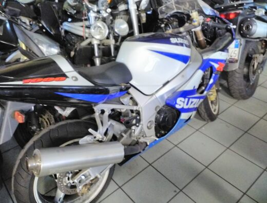 Moto Suzuki GSX-R 1000 di colore bianco e blu, parcheggiata in un garage con altre moto. JollyMoto s.n.c offre vendita e assistenza per moto e accessori.
