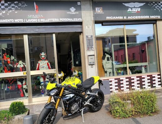 Negozio JRD e SPARTA CUSTOM GEAR BY ASR MOTO con moto giallo-nera parcheggiata di fronte. Vetrina con abbigliamento moto, caschi e accessori in esposizione. Servizi di personalizzazione abbigliamento e vendita ricambi moto visibili.