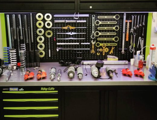 Banco da lavoro di Judmax Motorsport con attrezzi, sospensioni, molle e accessori per la manutenzione e riparazione di moto.