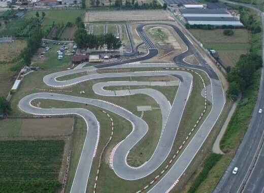 Vista aerea del Kartodromo di Casaluce, Italia, con pista tortuosa, edifici di supporto, parcheggio, vegetazione circostante e strada adiacente