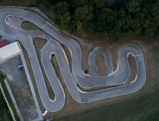 Vista aerea del Kartodromo Planet Kart, una pista sinuosa per noleggio go-kart e moto, circondata da vegetazione e con edifici di servizio.