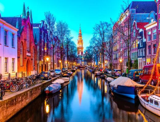Suggestiva vista notturna di un canale di Amsterdam, Paesi Bassi, con riflessi luminosi sull'acqua e architettura storica.