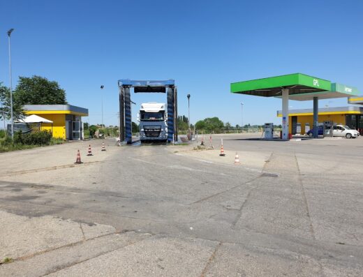 A white truck is being washed at the Kazmi Truck & Car Wash facility, located next to a gas station on a sunny day.