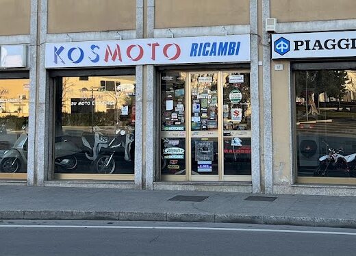 Facciata del negozio Kosmoto Ricambi Olbia S.A.S., rivenditore di moto, scooter, ricambi e accessori Piaggio e SYM, con vetrine espositive e insegne ben visibili.