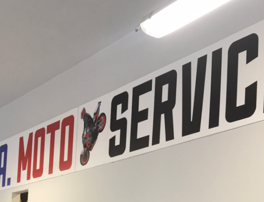 Insegna di L.A. Moto Service con l'immagine di una moto da cross impennata. Servizi e accessori per motociclisti.