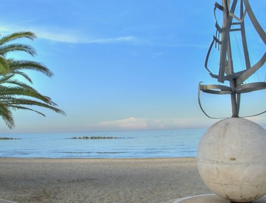 Scultura moderna sulla spiaggia di La Casa Blanca, con una palma e vista sul mare Adriatico. Installazione artistica con sfera e design nautico.