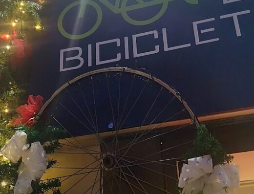 L'ingresso de La Casa della Bicicletta e Moto Elettrica addobbato con una ruota di bicicletta decorata a festa, vetrina di accessori e e-bike.