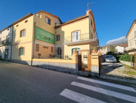 La Casa di Michele B&B, a yellow building with a balcony and a sign, located in a residential area with a car parked in the driveway.