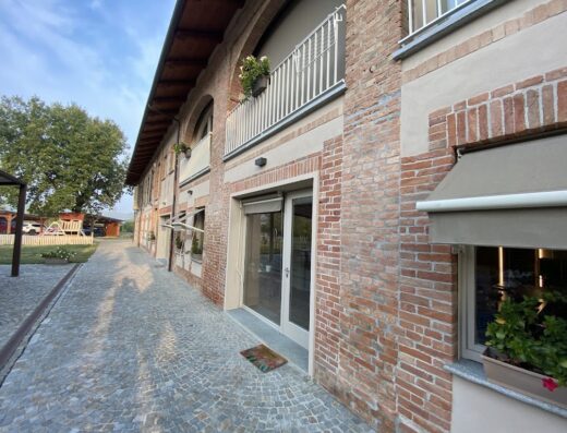 La Cascina di Carlotta 1846: dettaglio esterno della struttura con facciata in mattoni, balcone fiorito e pavimentazione in pietra. Un luogo di charme.