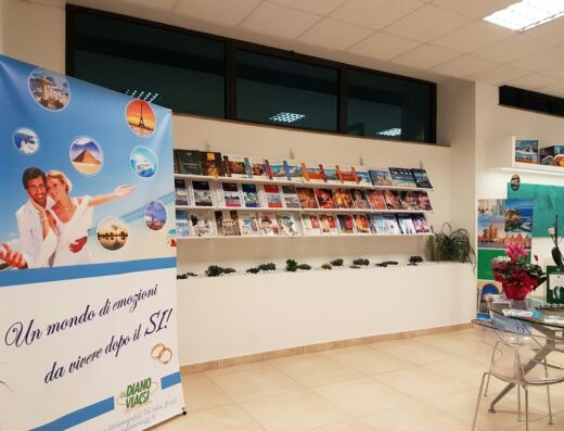 Interno dell'agenzia La Diano Viaggi Tour Operator con banner promozionale "Un mondo di emozioni da vivere dopo il SI!" e scaffale con cataloghi di viaggi.