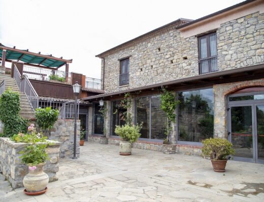 La Foresteria di San Leo: vista esterna della struttura in pietra con terrazza panoramica accessibile tramite scale, ampie vetrate e area esterna pavimentata e curata.