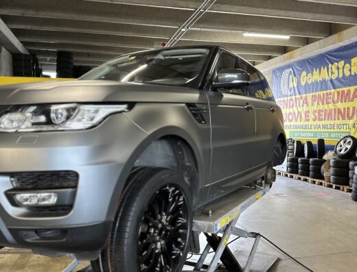 La Gommisteria: SUV grigio opaco su ponte elevatore per cambio pneumatici. Servizio di vendita gomme nuove e usate. Accessori e manutenzione auto.