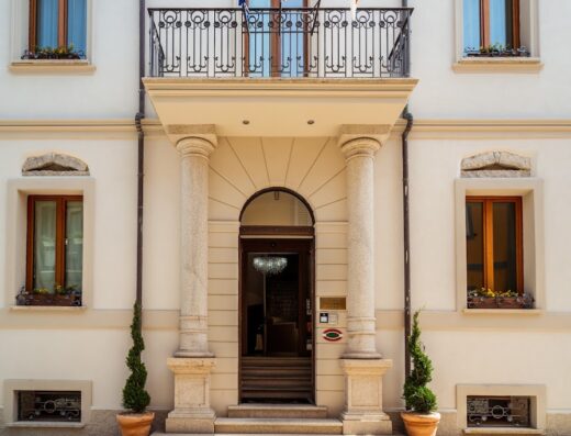 La Locanda del Conte Mameli, hotel di charme a Olbia: dettaglio dell'entrata principale con colonne in pietra, balcone in ferro battuto e finestre fiorite.