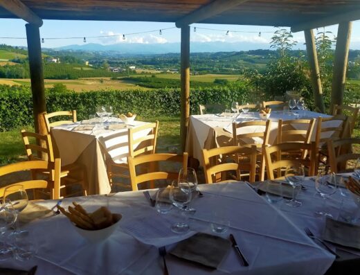 Tavoli apparecchiati all'aperto a La Locanda del Nocciolo con vista panoramica sulle colline e le montagne sullo sfondo.