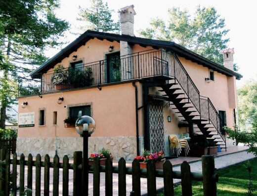 La Maga del Lago: edificio a due piani con scala esterna in ferro battuto, balcone, recinzione in legno e giardino curato, ideale per motociclisti in viaggio