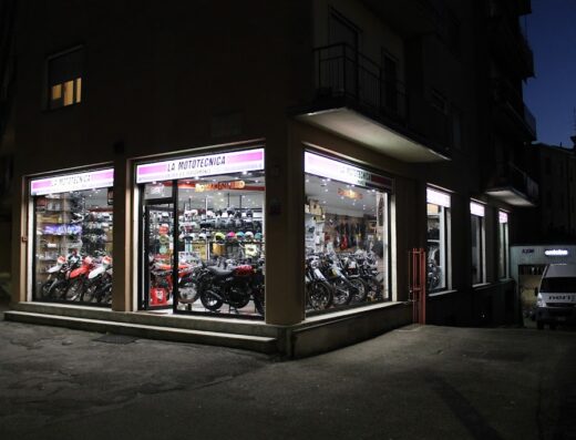 La Mototecnica s.n.c. di Eugenio Neri e C.: vetrina illuminata di negozio di moto con esposizione di motociclette Royal Enfield, caschi e accessori per motociclisti.