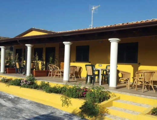 La Pietra Bianca: Facciata esterna di una casa colonica gialla con portico, colonne bianche, tavoli e sedie; ideale per un soggiorno rilassante.