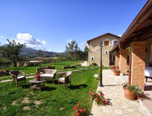 Un'accogliente area relax esterna a La Rosa nel Bicchiere, con mobili in vimini su un prato verde e vista panoramica sulle colline circostanti.