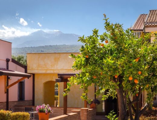 La Terra Dei Sogni Country Hotel: vista esterna con albero di arance, architettura colorata e sfondo del vulcano Etna, Sicilia.