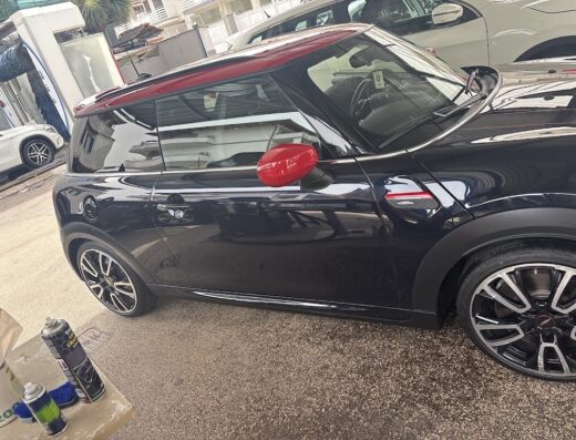 Auto Mini Cooper nera con tetto e specchietti rossi a Lampitelli's CarWash, in attesa di lavaggio e pulizia professionale.
