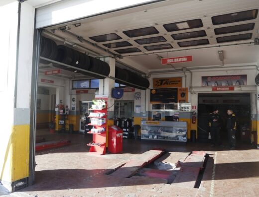 Interno di un'officina BestDrive con ponte sollevatore, scaffali di prodotti, pneumatici stoccati e personale. Servizi di riparazione e sostituzione gomme.