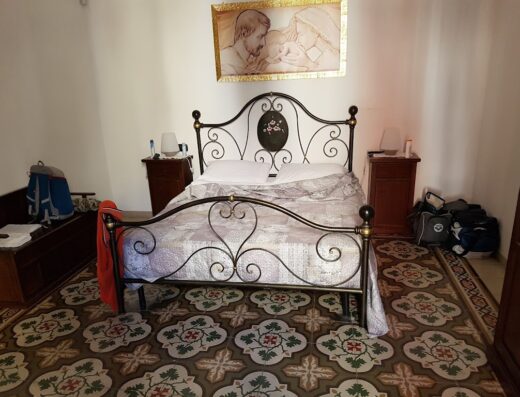 Camera da letto matrimoniale all'Angolo Antico, con letto in ferro battuto, comodini in legno, pavimenti decorati e quadro a parete.