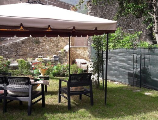 L'angolo fiorito: un'area relax all'aperto con tavolo e sedie sotto un gazebo, circondata da un giardino curato con fiori e piante ornamentali.