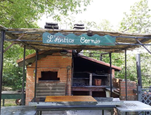 L'Antico Cornio features a brick oven and grill under a wooden structure, perfect for motorcycle enthusiasts and travelers seeking authentic Italian cuisine.