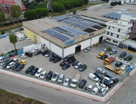Veduta aerea del centro riparazioni Lanza, con pannelli solari sul tetto e parcheggio pieno di auto, furgoni e camioncini.