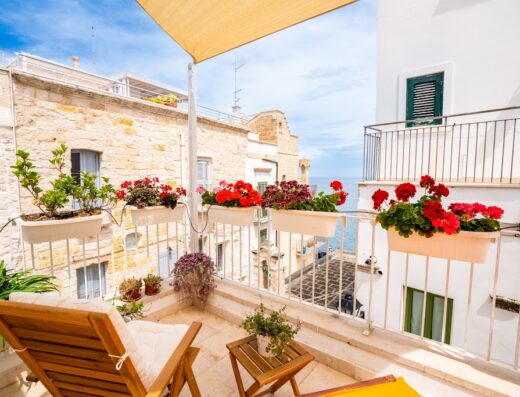Balcone fiorito con vista mare in Puglia, arredato con sdraio in legno e tavolino, ideale per relax e vacanze nella casa sul mare L'Arco Antico.