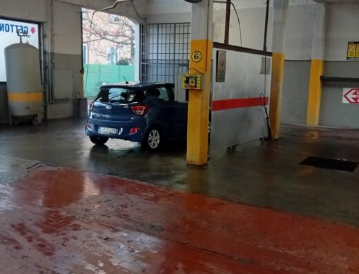 Interno di L'Auto Moto Lavaggio Car & Bike Wash, con un'auto blu pronta per il lavaggio, pavimento bagnato e attrezzature professionali.