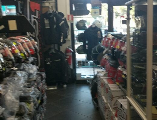 Interno del negozio L'Autoaccessorio Imperia, con espositori di caschi, giacche e accessori per moto, illuminazione interna e pavimenti scuri.